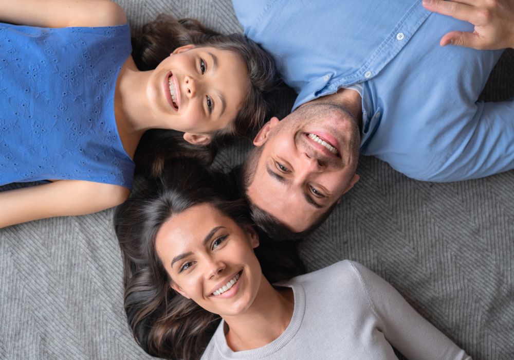 Imagen desde arriba de una familia tumbada en la cama. La imagen representa salud y bienestar.